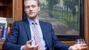 Young, polished man in a suit holding a whiskey glass—satirical nod to overconfident experts who complicate simple solutions.