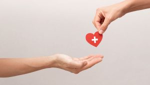 Symbolic image of life insurance legacy gift — one hand passing a red heart with a white cross to another, representing charitable giving