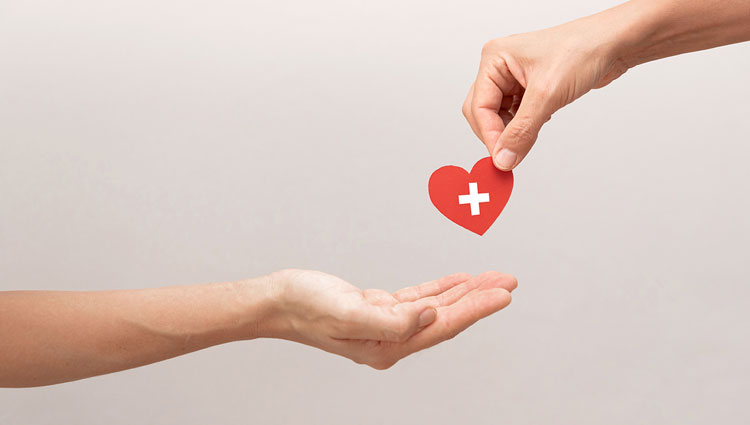 Symbolic image of life insurance legacy gift — one hand passing a red heart with a white cross to another, representing charitable giving