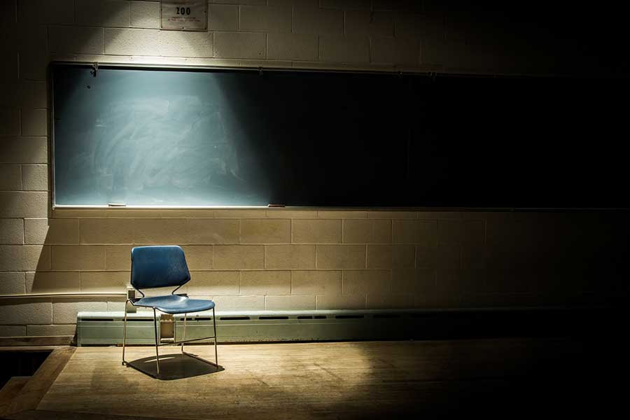 An image of an empty chair in front of a blackboard. A spotlight shines on the chair, to illustrate the concept "Get unstuck and get moving."