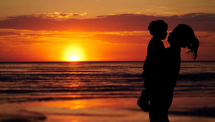 Mother carrying daughter at sunset on the beach