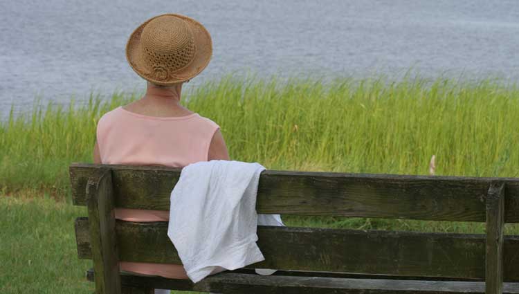 Woman sitting on bench in front of a lake contemplating and dreaming