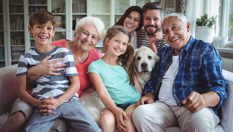 Gathered family and children with dog in the middle all sitting on a sofa