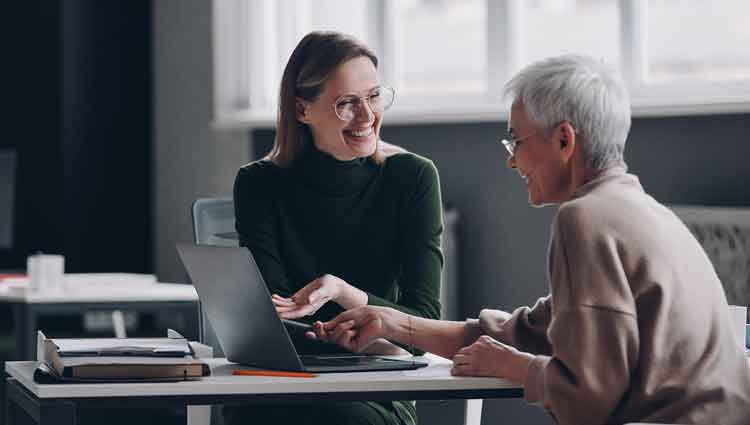 A picture of two white women sitting at a desk and chatting, to illustrate a PlannedGiving.Com post about having an effective planned giving conversation.