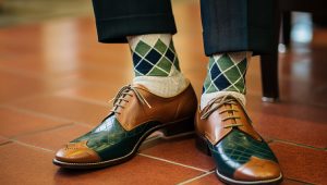 Person wearing green and navy argyle socks with brown dress shoes on tile floor