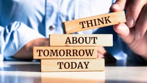 Business professional stacking four wooden blocks on reflective surface that read 'THINK ABOUT TOMORROW TODAY', illustrating the importance of future planning in charitable giving.