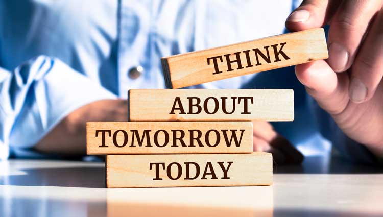 Business professional stacking four wooden blocks on reflective surface that read 'THINK ABOUT TOMORROW TODAY', illustrating the importance of future planning in charitable giving.
